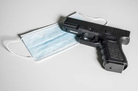 Pistol gun laying on top of medical mask in concept for dangers faced by front line medical personnelの写真素材