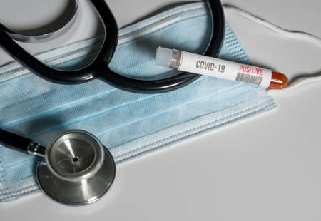 Positive blood test for Coronavirus laying on doctor surgical mask with stethoscope to show danger to front line medical workersの写真素材