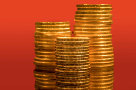 Focus on a stack of gold coins with other coin stacked in the background out of focus against red backdropの写真素材