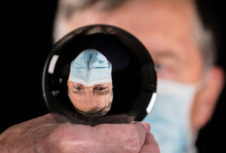 Senior man wearing face mask against coronavirus and reflected in fortune telling glass ball. Concept of people choosing responsibility in electionの写真素材