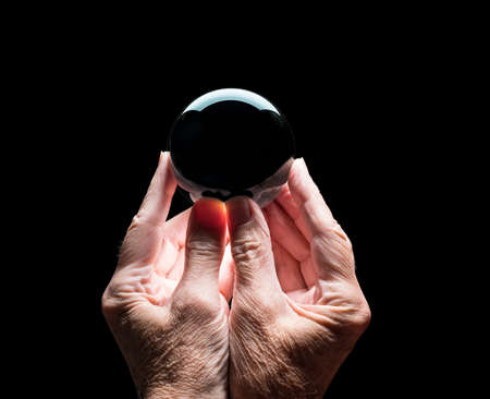Senior caucasian hands holding a crystal futures or fortune telling ball with black center to allow...