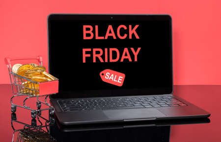 Concept for online Black Friday and winter sales with shopping cart filled with gold coins in front...