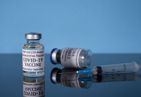 Small bottle of coronavirus vaccine on reflective glass table with syringe ready for vaccination