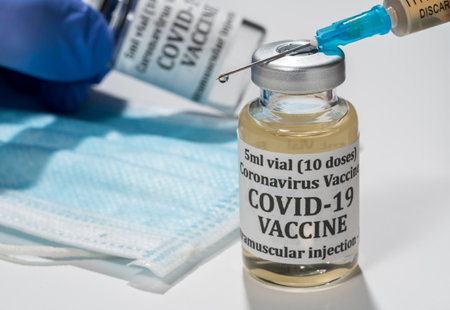 Covid-19 coronavirus vaccine with hypodermic syringe needle with droplet of liquid on tip. Gloved...