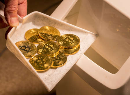 Brushing bitcoins into a dustpan as concept for the collapse in value of cyber coins and digital currencyの写真素材