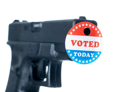 Concept for election violence with handgun decorated with I voted today sticker with hole made by...