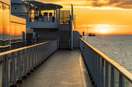 Sun setting over the water horizon with a cruise ship in the foreground and bulk carrier cargo ship behindの写真素材