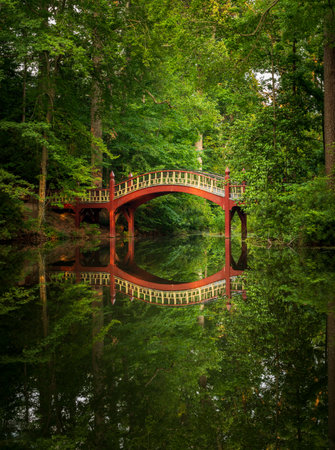 Ornate wooden bridge over very calm Crim Dell pond on campus of William and Mary college in Williamsburg Virginiaの写真素材
