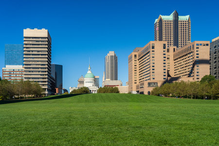 View across green lawn of Gateway Arch National Park with other office buildings in downtown cityscapeの写真素材