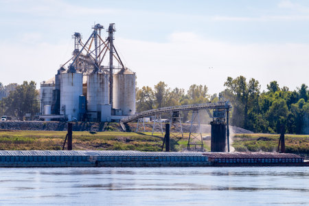 Tugboat pushing freight barges past grain loading dock in farming country in Kentuckyの写真素材