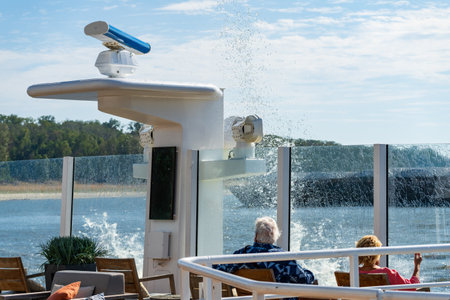 Spray and wave from passing freight barge creates splash onto deck of a modern Mississippi river cruise boatの写真素材