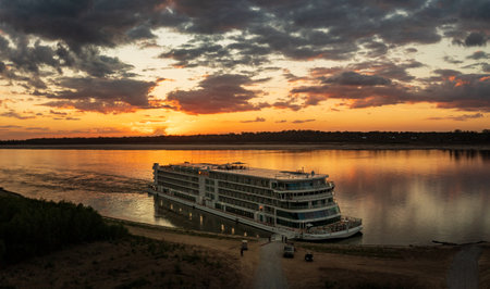 Vicksburg, MS - 25 October 2023: Viking Mississippi docked by bank as sunset cast golden glow on the boat and reflectionsのeditorial素材