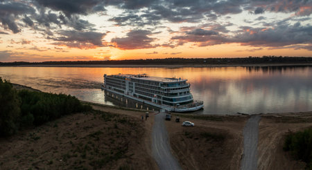 Vicksburg, MS - 25 October 2023: Viking Mississippi docked by bank as sunset cast golden glow on the boat and reflectionsのeditorial素材