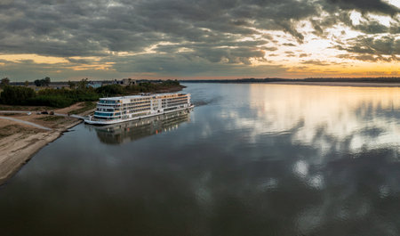 Vicksburg, MS - 25 October 2023: Viking Mississippi docked by bank as sunset cast golden glow on the boat and reflectionsのeditorial素材