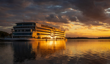 Vicksburg, MS - 25 October 2023: Viking Mississippi docked by bank as sunset cast golden glow on the boat and reflectionsのeditorial素材