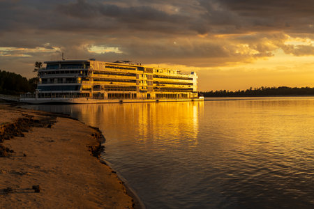 Vicksburg, MS - 25 October 2023: Viking Mississippi docked by bank as sunset cast golden glow on the boat and reflectionsのeditorial素材