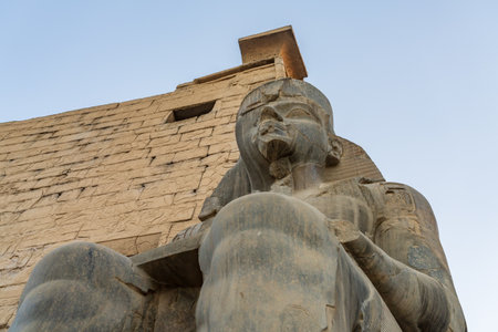 A massive stone statue of Ramesses II stands in Luxor temple, showcasing intricate carvings under the warm glow of the setting sun.の写真素材