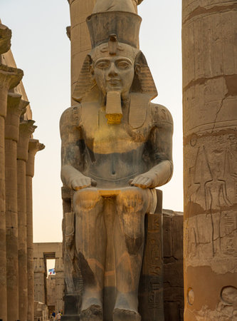 A massive stone statue of Ramesses II stands in Luxor temple, showcasing intricate carvings under the warm glow of the setting sun.の写真素材