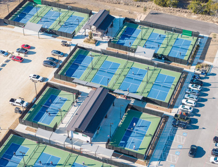 Aerial view of a vibrant pickleball complex, numerous courts filled with players, surrounded by ample parking and lush greenery.の写真素材