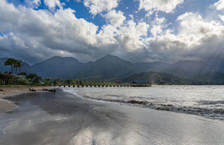 Hanalei Pier and beach are framed by dramatic mountains and sky in this scenic view of the north shore of Kauai.の写真素材