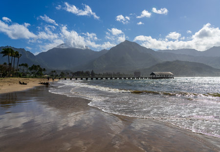 Hanalei Pier and beach are framed by dramatic mountains and sky in this scenic view of the north shore of Kauai.の写真素材