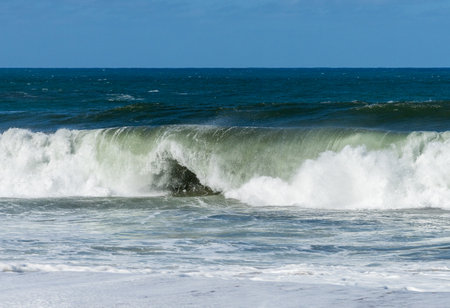 Ocean waves crashing on the shore under a blue sky, with the turquoise water rippling and splashing.の写真素材