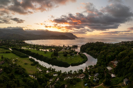 A vibrant aerial view of sunset clouds over the lush landscape of Hanalei Bay, framed by majestic mountains in Kauai, Hawaii.の写真素材