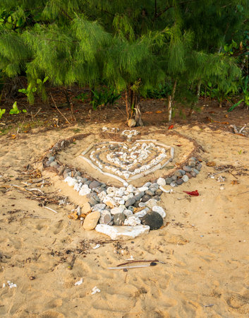 Heart made of rocks on sandy beach in Kauai with evergreen tree as backdrop displaying a symbol of love, or perhaps marriage proposal.の写真素材