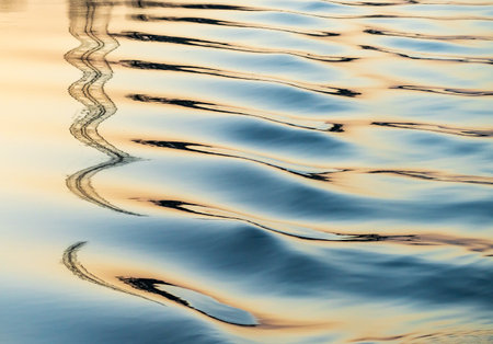 Ripples in river from cruise boat provide abstract reflections of pylon on bank at sunsetの写真素材