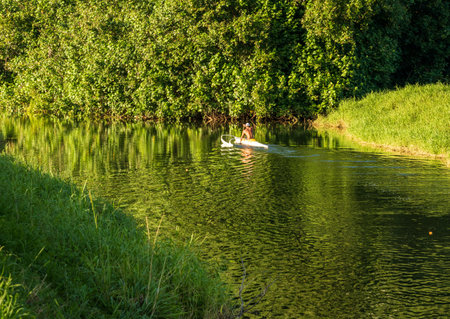 A man paddles a traditional Hawaiian outrigger canoe through the tranquil waters of Hanalei River on a sunny day, creating mirrored reflections.の写真素材
