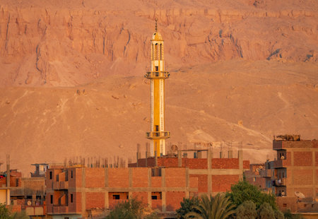 Minaret at sunset with home construction and large sand mountain of Sahara desert by banks of Nile Riverの写真素材