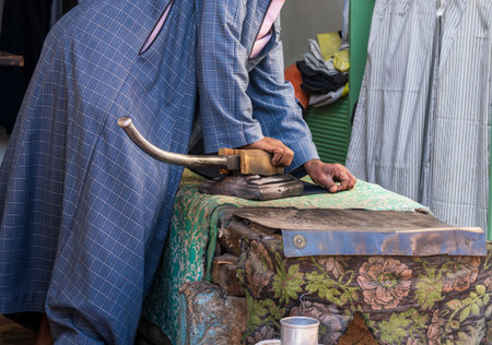 A tailor skillfully uses a foot-operated iron to smooth material in Esna, Egypt, showcasing traditional tailoring techniquesの写真素材
