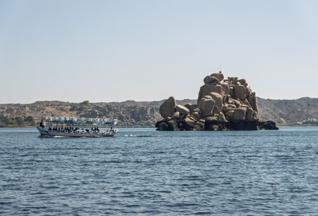 Tourists in ferry boat passing rocky island on way to Philae Temple in Aswan reservoirの写真素材