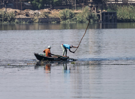Two men in their small boat on a calm river while tending to fishing net in the waterの写真素材