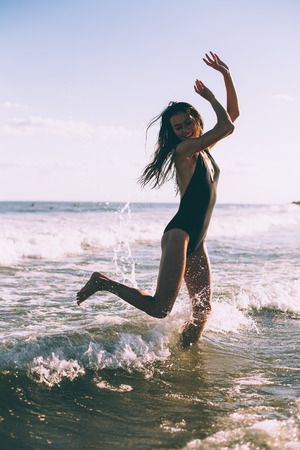 A girl is black swimsuit is jumping in the seaの写真素材