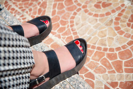Female feet in black sandals and red nails