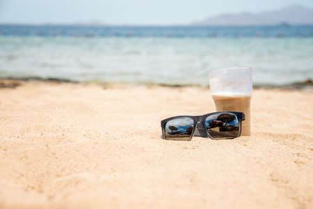 sunglasses and glass on the sand near the seaの写真素材