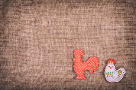 toy rooster and chicken on a brown fabric backgroundの写真素材