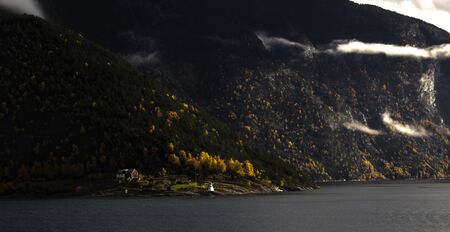 Farm and lighthouse on the shore of autumn fjord with low cloudsの写真素材