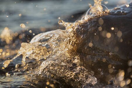Closeup photo of sea waves braking on a wet seashore stones summer sunset, water splashes , sun...