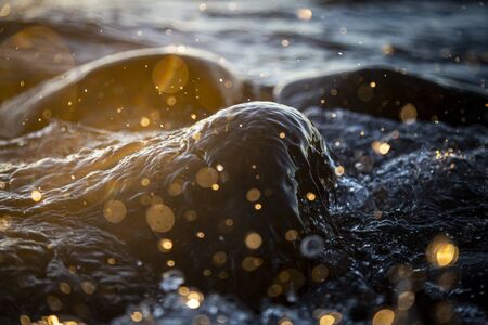 Closeup photo of sea waves braking on a wet seashore stones summer sunset, water splashes , sun...