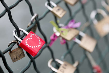 Closeup on a red padlock with a studded heart on a bridge railing  Selective focus on the red padlock の写真素材