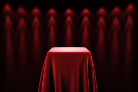 Presentation pedestal covered with a red silk cloth in front of a wall illuminated by spot lightsの写真素材