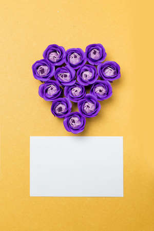 Heart-shaped rose soap flowers and white card on yellow backgroundの写真素材