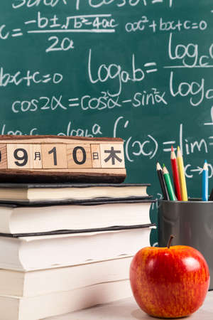 Apple, books and pencils on desk with blackboard in the background