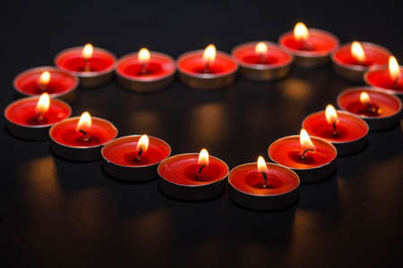 Burning heart-shaped candles on black background