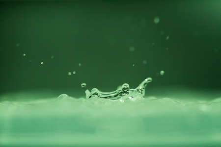 droplet fell into water with splash on green backgroundの写真素材