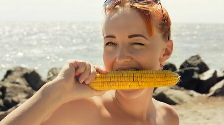 Funny woman eating boiled corn on the beachの写真素材
