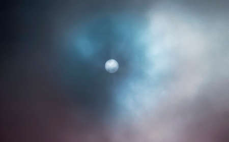 A moody picture of a blue full moon against a dark and cloudy sky