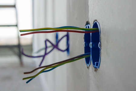 Several colored electrical wires sticking out of a new wall on a construction site